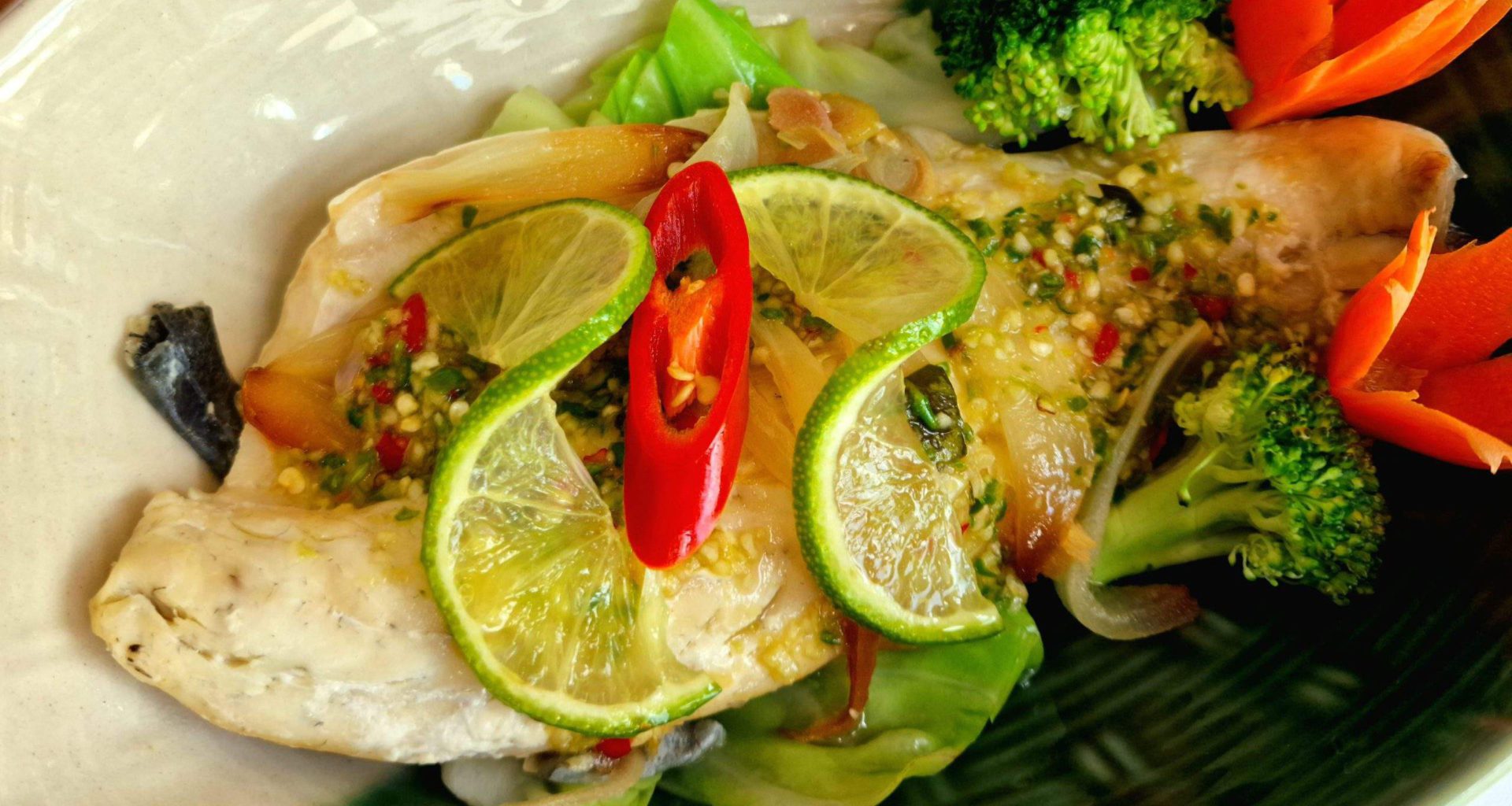 Steamed seabass fillet in a two tone dish served with dressing and two line slices on top. One Thai